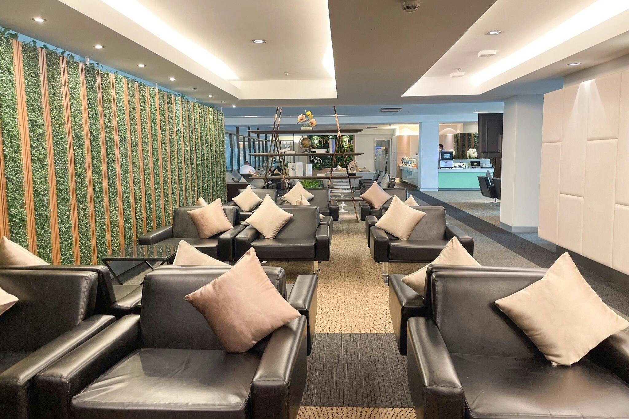 A modern lounge area with black armchairs, beige cushions, and decorative plants under warm ceiling lighting.