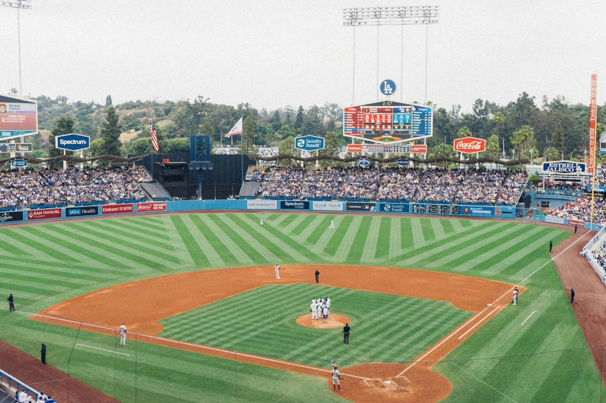 A baseball game in progress at a stadium with spectators, featuring a mound visit at the center of the field.