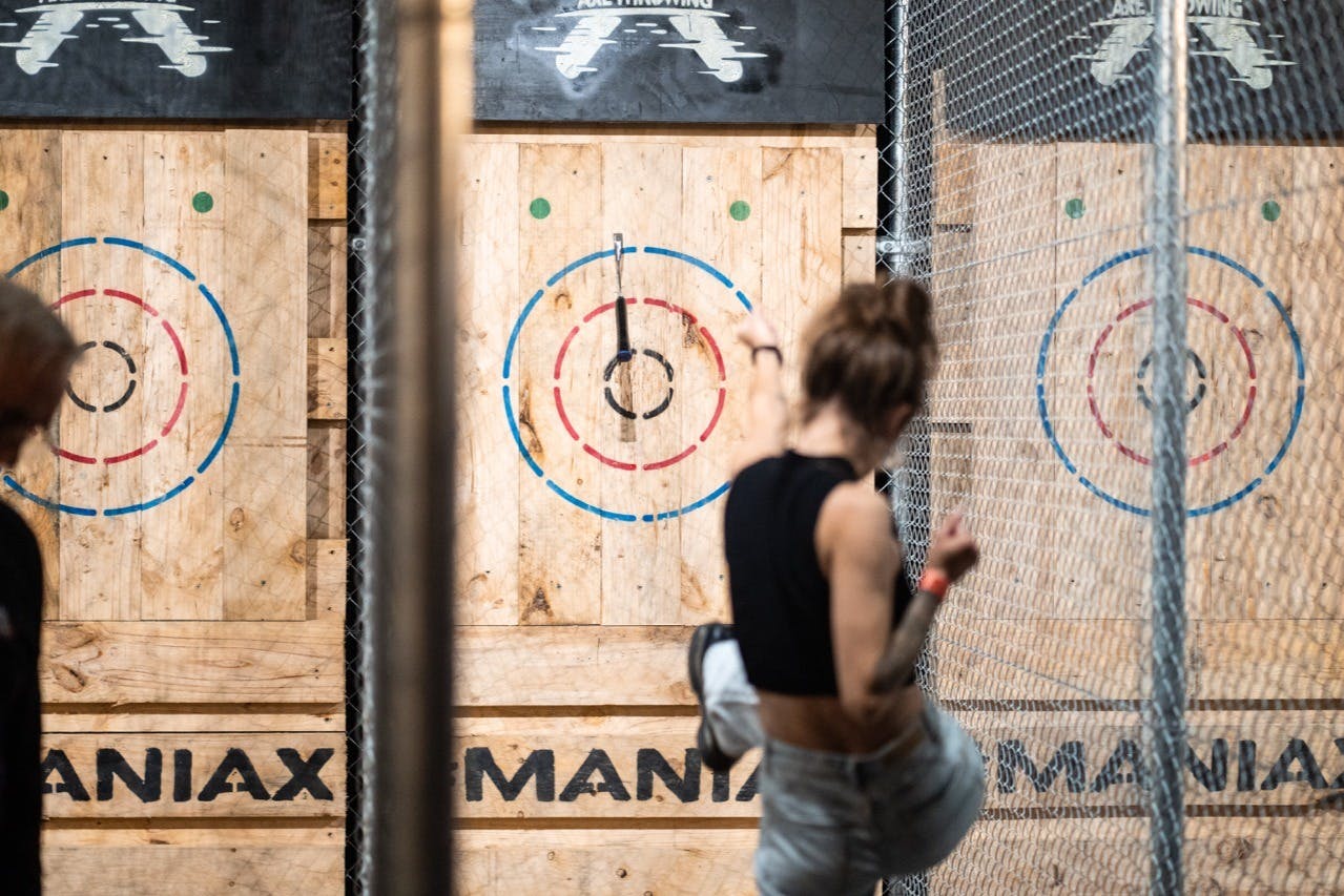 A person throwing an axe at a target in an axe-throwing venue with wooden targets and chain-link dividers.
