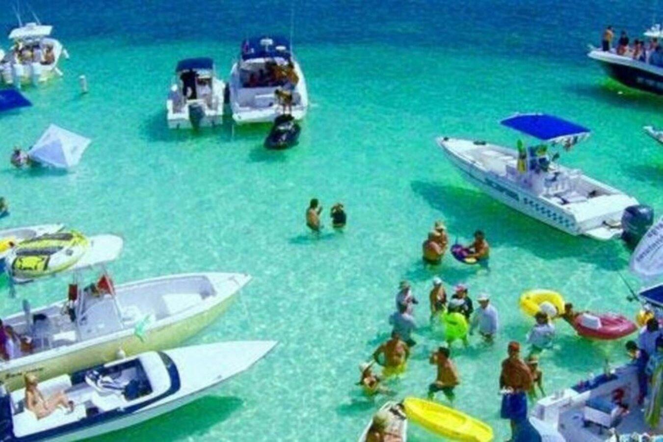Crystal-clear waters, boats gently floating, and people wading in shallow bliss—an idyllic scene of serene relaxation