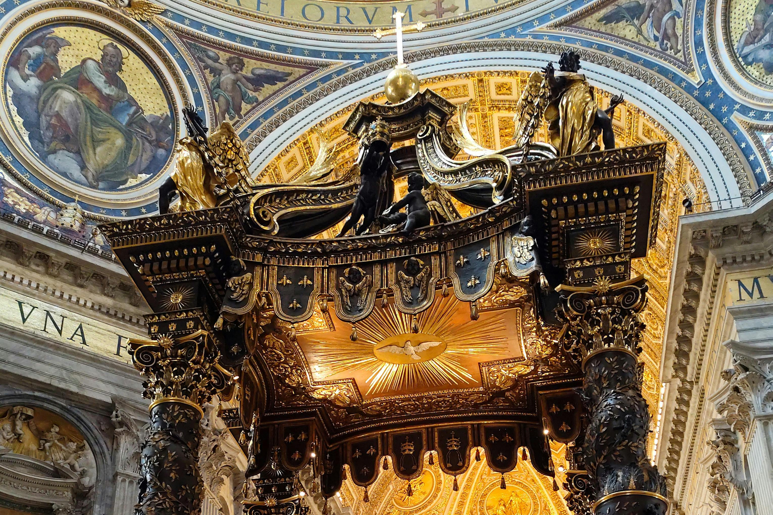 Ornate golden and black canopy with intricate details inside a richly decorated domed building.