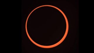 un anillo de luz naranja que es el sol, está sobre un fondo negro.
