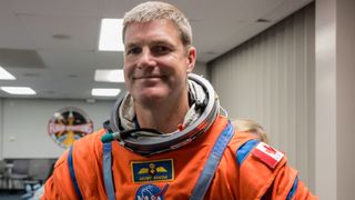 Jeremy Hansen con un traje espacial naranja sonriendo en una instalación de la NASA