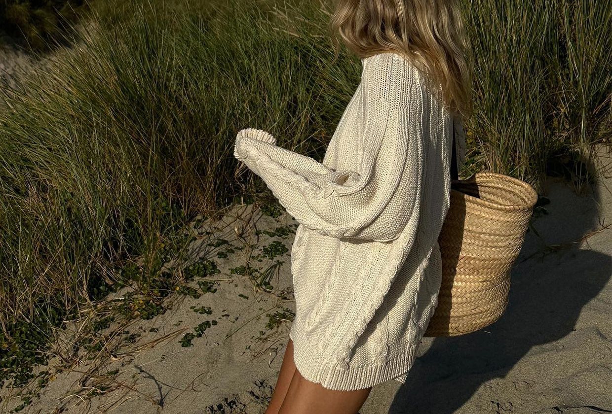 Lucy Williams wearing a loose cotton sweater with a straw bag on the beach.