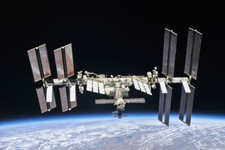 Una gran estación espacial en forma de H con paneles solares en forma de alas flota sobre una Tierra azul y blanca.