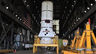 El segmento inferior de un propulsor de cohete sólido blanco se encuentra sobre un soporte amarillo dentro de un hangar de cohetes gigante.