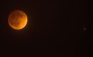 la luna aparece roja junto a una estrella azul brillante en el cielo