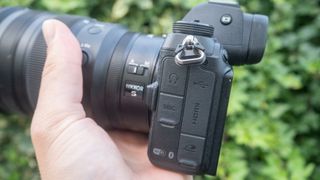 Una foto de la Nikon Z6 II sostenida en una mano con hojas en el fondo.
