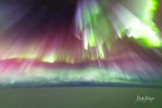 Cortinas de auroras verdes y magenta ricas llenan el cielo, con un manto de nubes debajo.