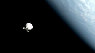 Una nave espacial blanca y cónica flota en la negrura sobre el espacio. Se puede ver una tierra azul y blanca a lo largo del borde más derecho de la foto
