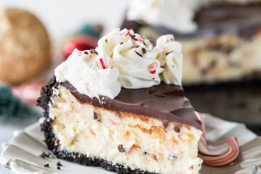 A slice of oreo crusted cheesecake, with peppermint and chocolate on top.