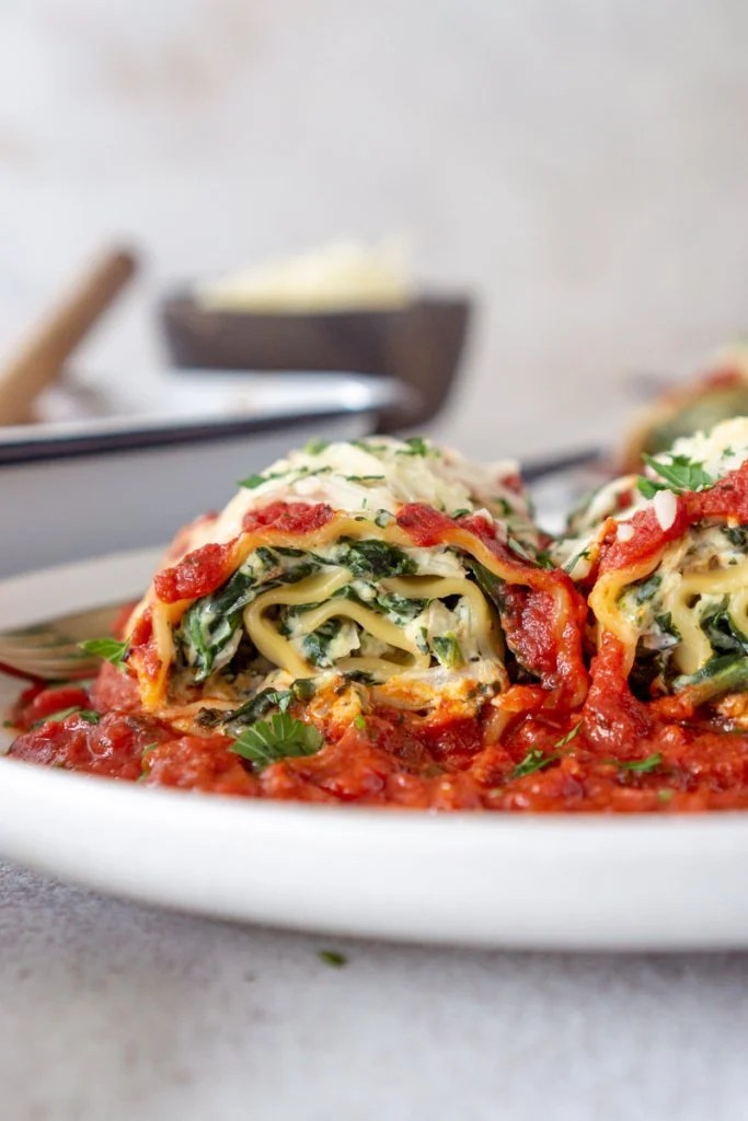 lasagna roll on a white plate with marinara sauce and a pan in the background
