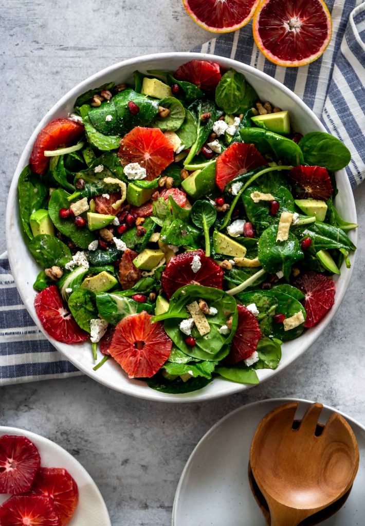 winter citrus green salad in a large bowl and sliced blood oranges off to the side
