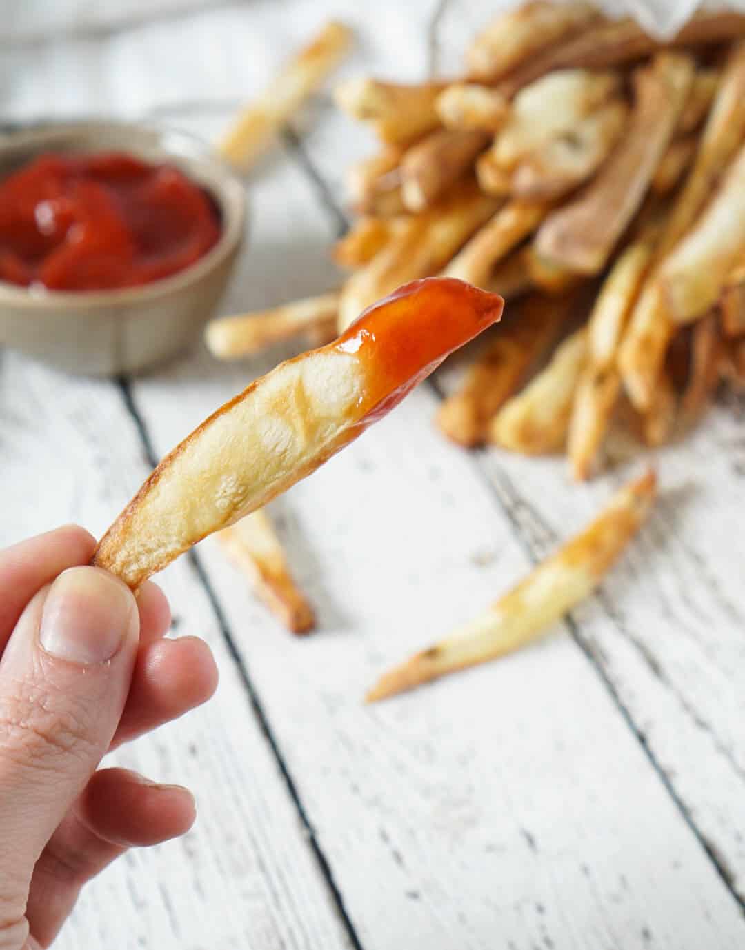 a hand holding a french fry dipped in ketchup