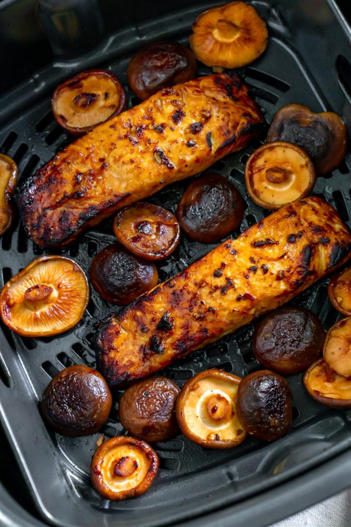 two salmon fillets with mushrooms in an air fryer basket