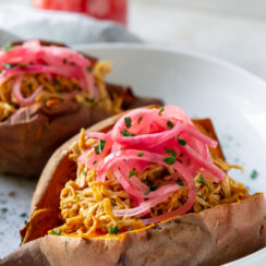 Bbq chicken stuffed sweet potato on a white plate next to a jar of pickled red onions.
