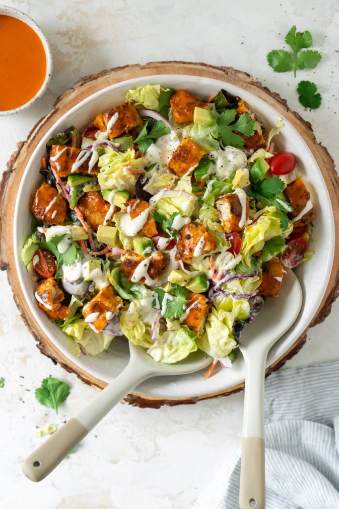 buffalo chicken salad in a salad bowl with tongs and a blue napkin