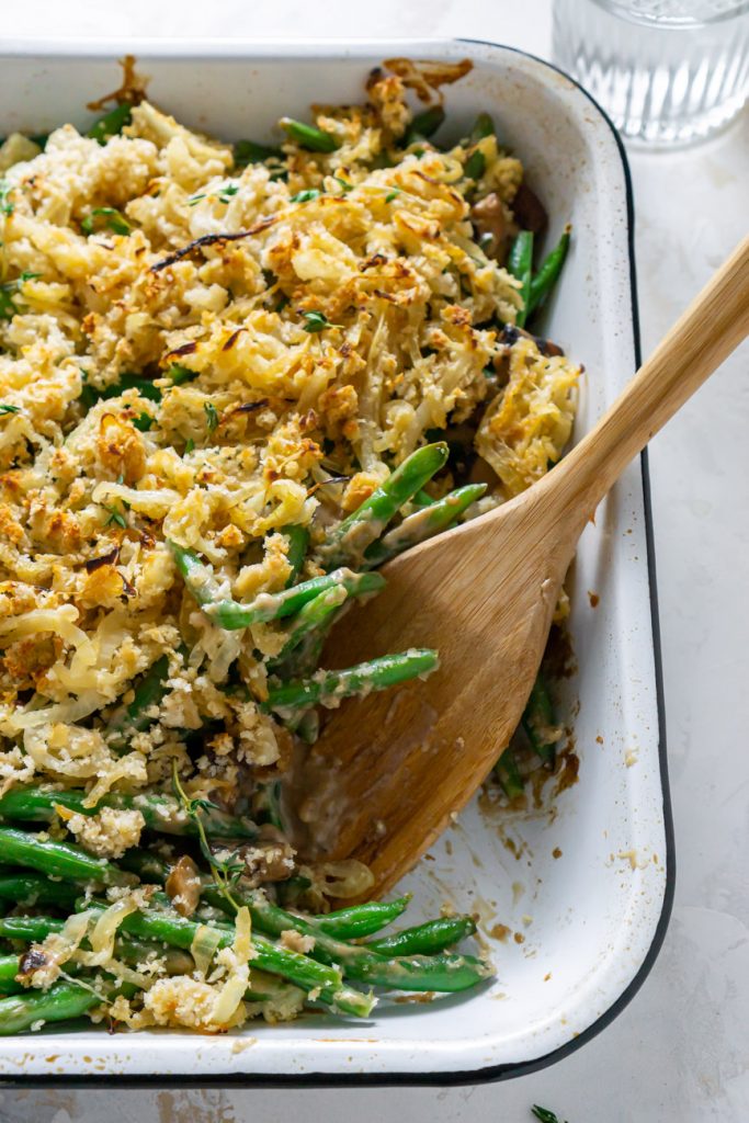healthy green bean casserole in a white baking dish with a wooden spoon