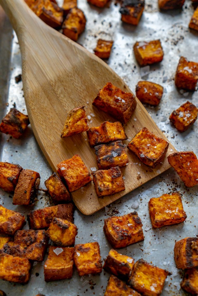 roasted sweet potatoes on a baking sheet with wooden turner