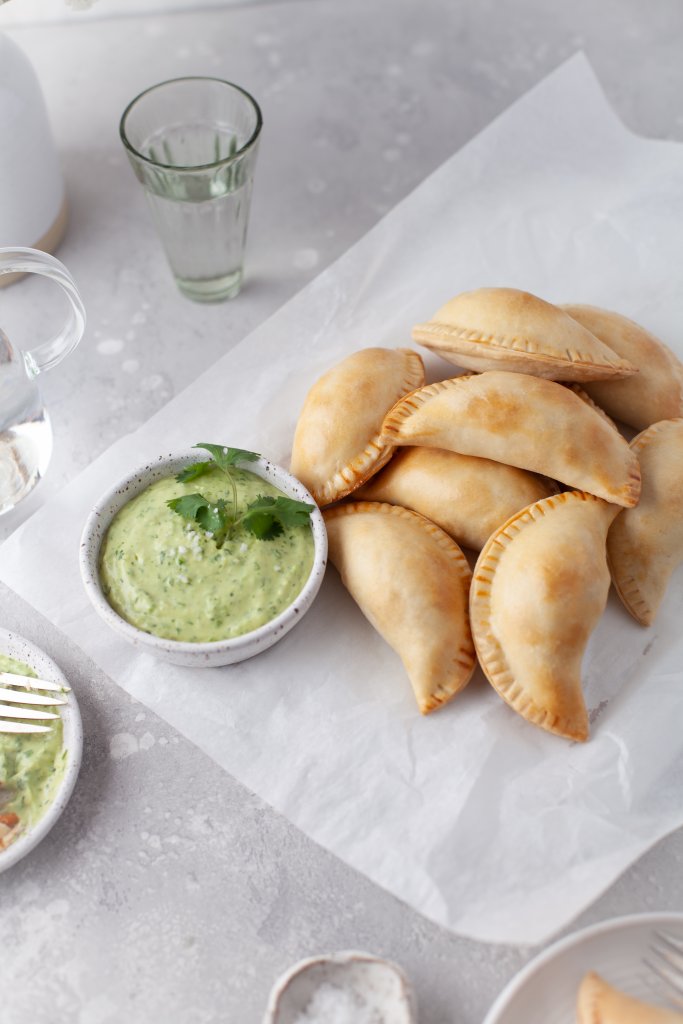 chicken empanadas on parchment paper with green empanada sauce