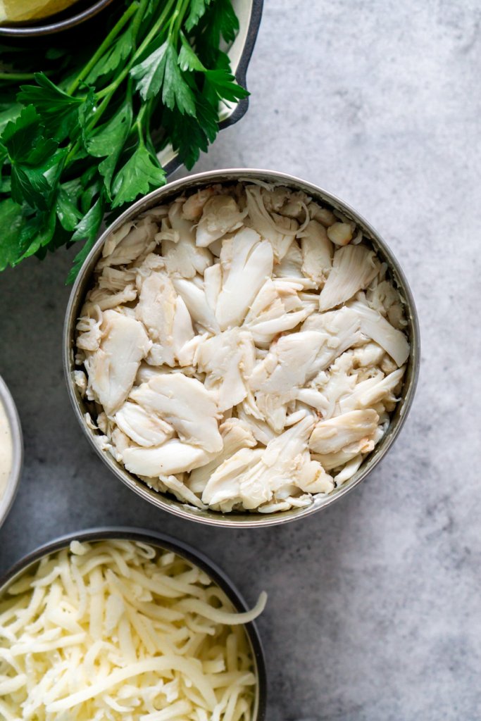 a can of jumbo lump crab meat with some parsley and shredded mozzarella cheese on the side.