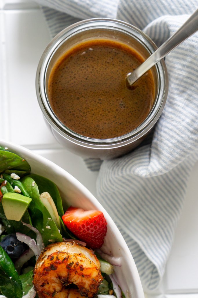 honey balsamic dressing in a glass jar with a silver spoon and a salad