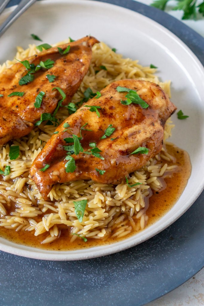two balsamic chicken breasts on a white plate with orzo