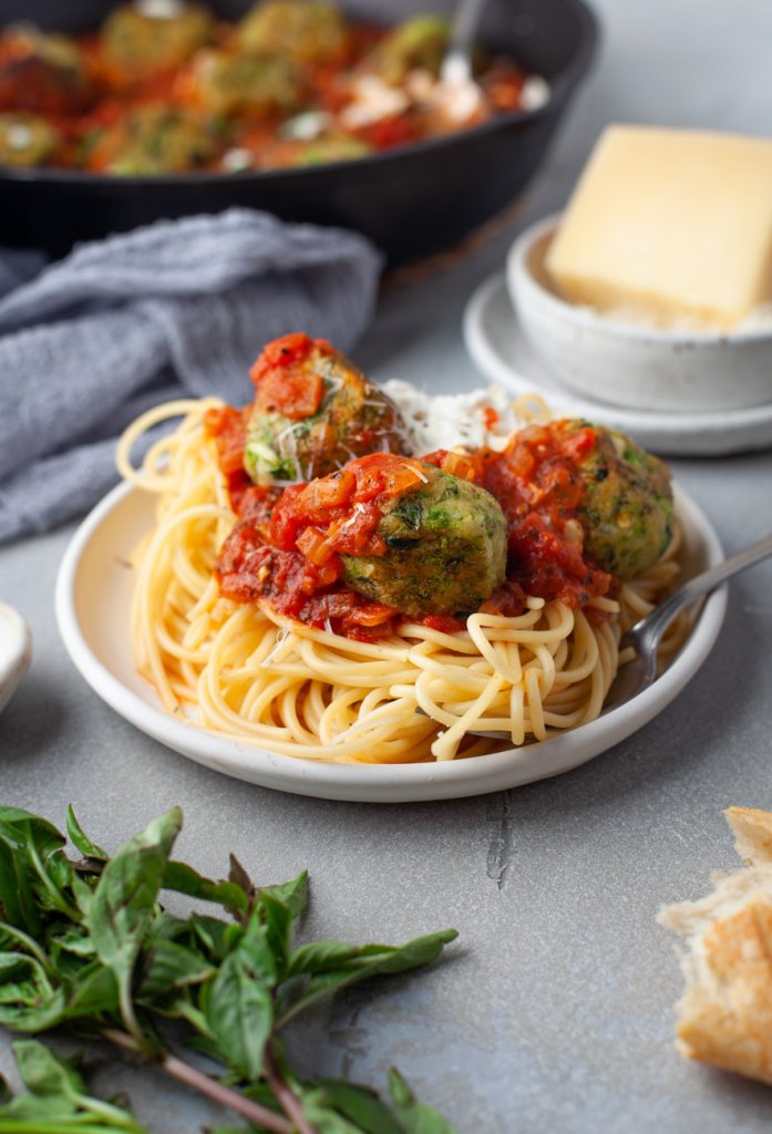 zucchini meatballs on a white plate with spaghetti, basil and cheese to the side