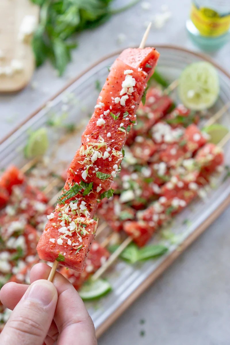 A hand holding a watermelon tajin skewer.