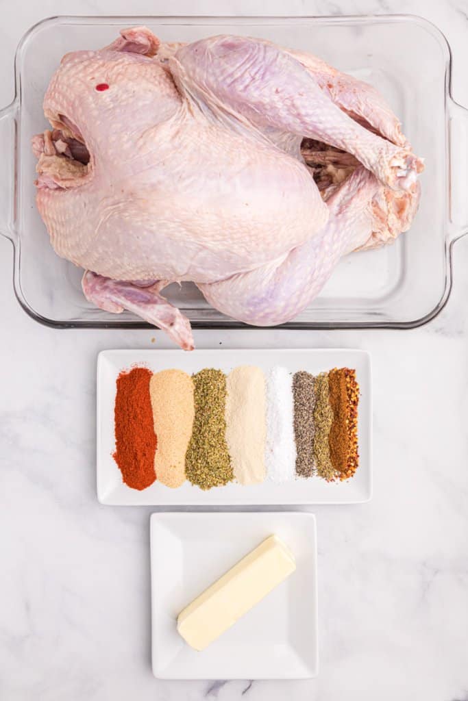 a turkey in a glass baking dish, spices on a white plate, and a stick of butter