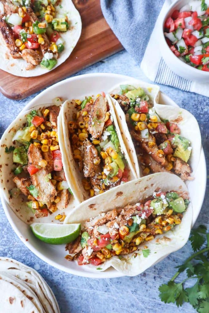 overhead of blackened chicken tacos with colorful toppings in mini flour tortillas and lime slice