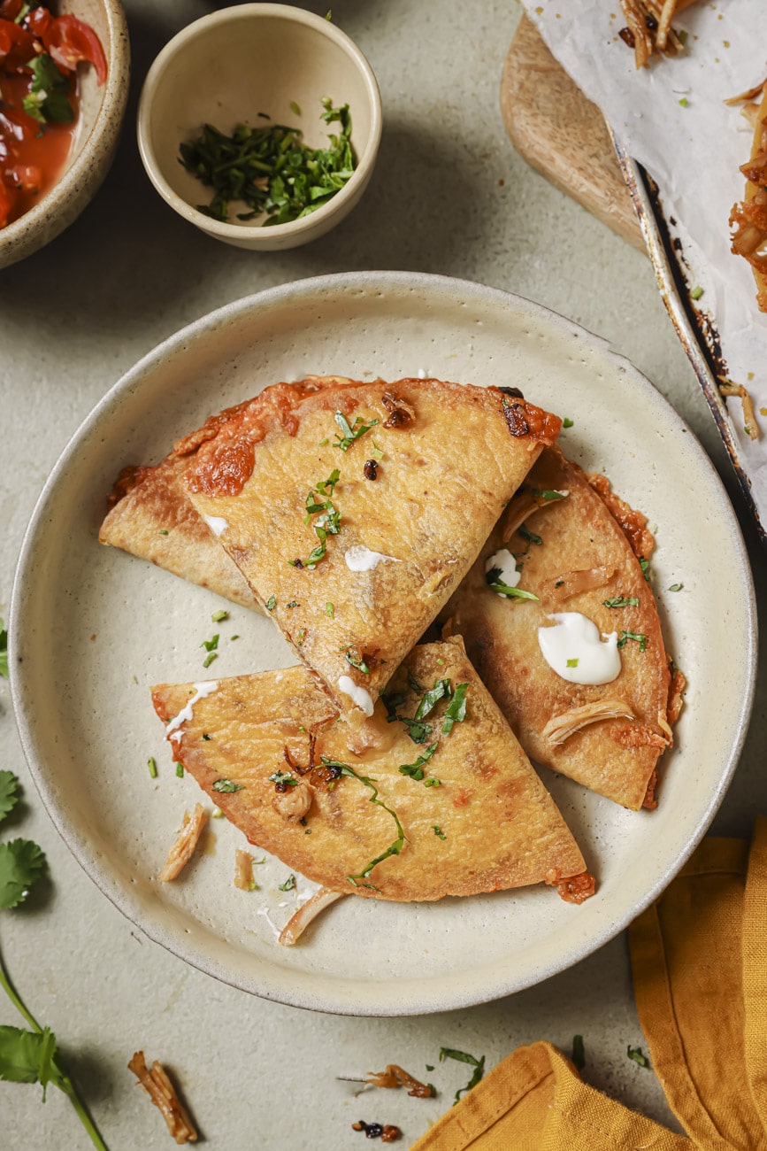 Four turkey quesadillas on a plate with with chopped cilantro on top and a few dollops of sour cream.