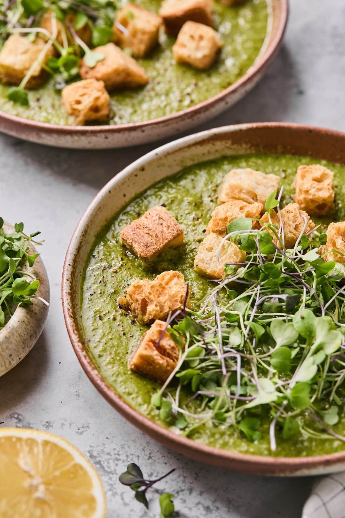 Two bowls of green soup with croutons and greens in brown bowls.