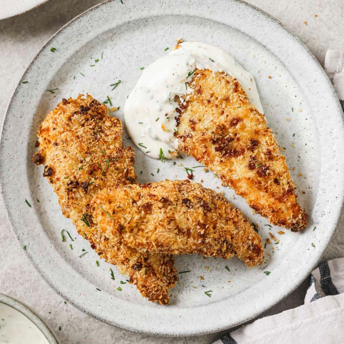 three crispy bacon ranch chicken tenders on a white plate with a dollop of ranch dressing