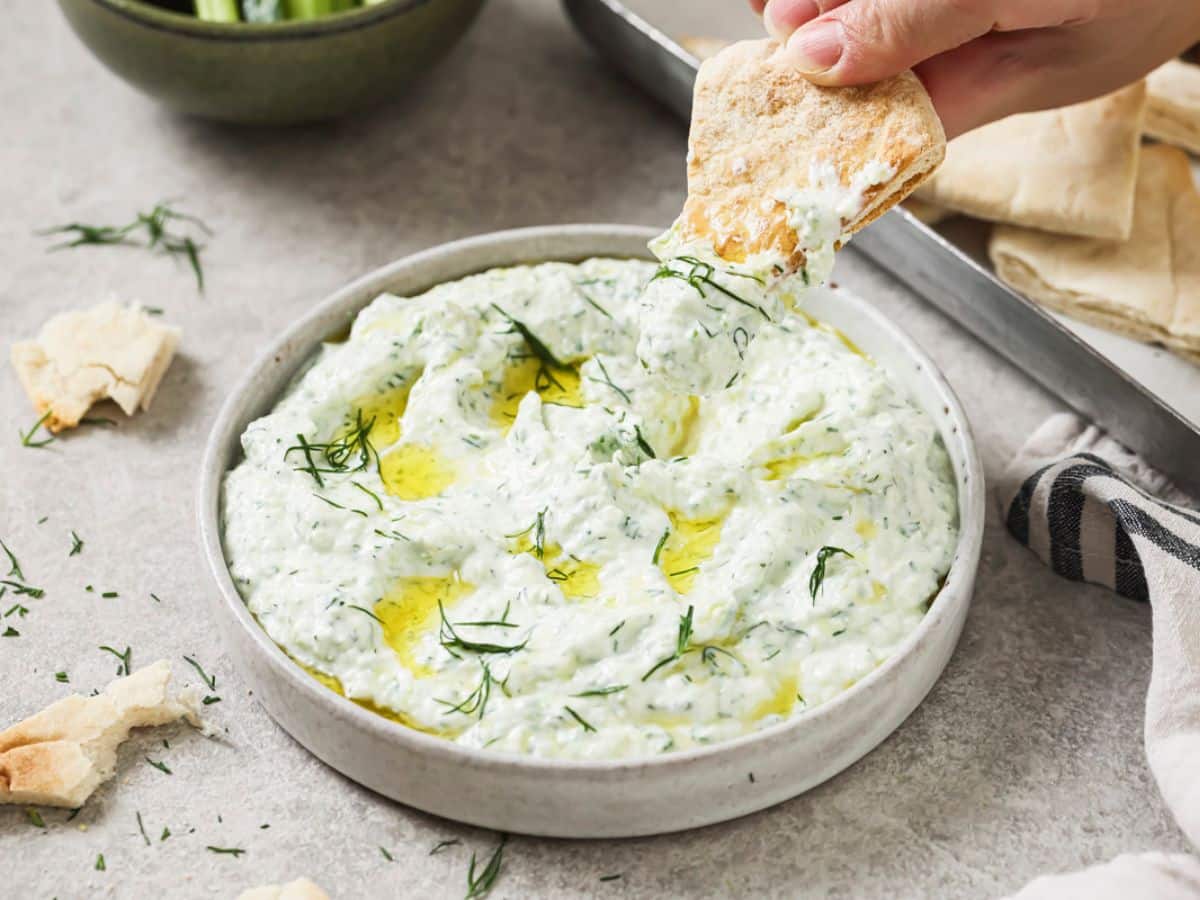 Dipping a piece of pita bread into a bowl of tzatziki sauce.