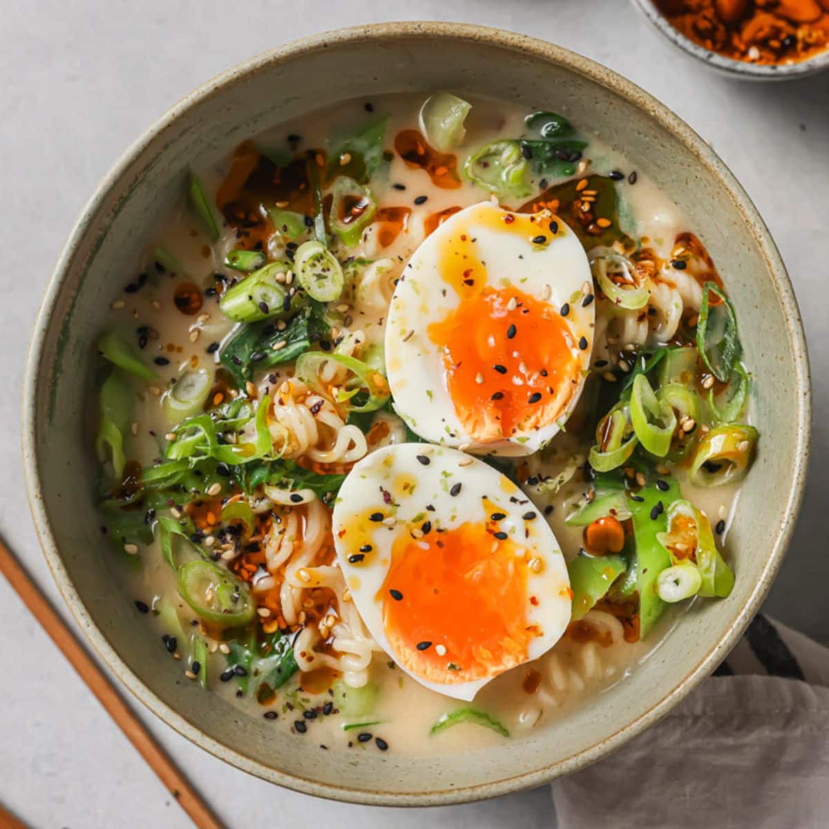 a bowl of spicy ramen topped with jammy eggs, sesame seeds, and furikake seasoning.