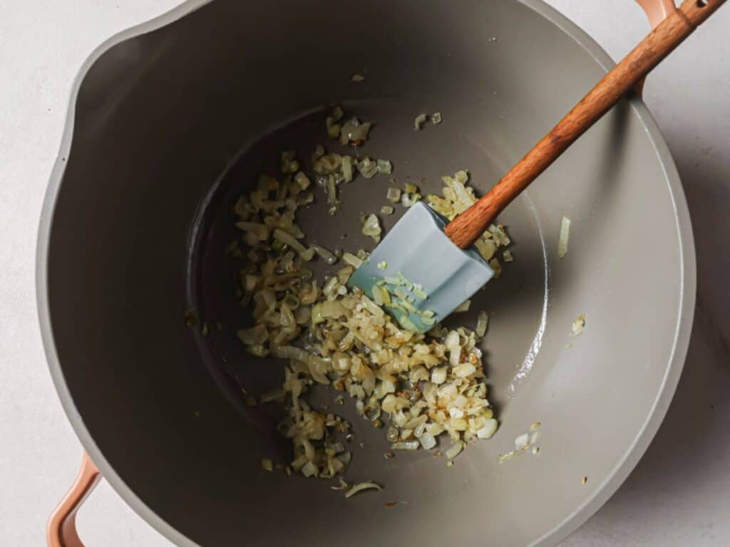 Diced onion, garlic, and sliced green onions sautéing in sesame oil in a large pot.