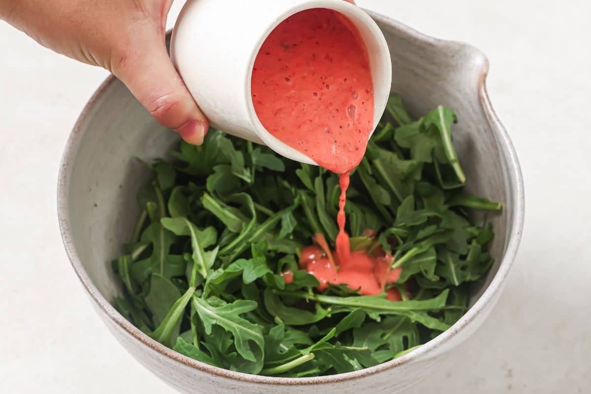 Pouring the strawberry dressing onto the arugula salad greens.