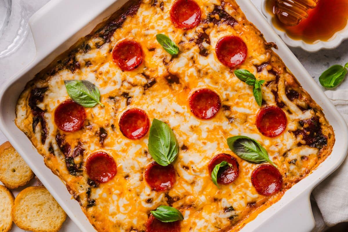 Hot honey pizza dip in a square baking dish topped with mini pepperoni and fresh basil. 