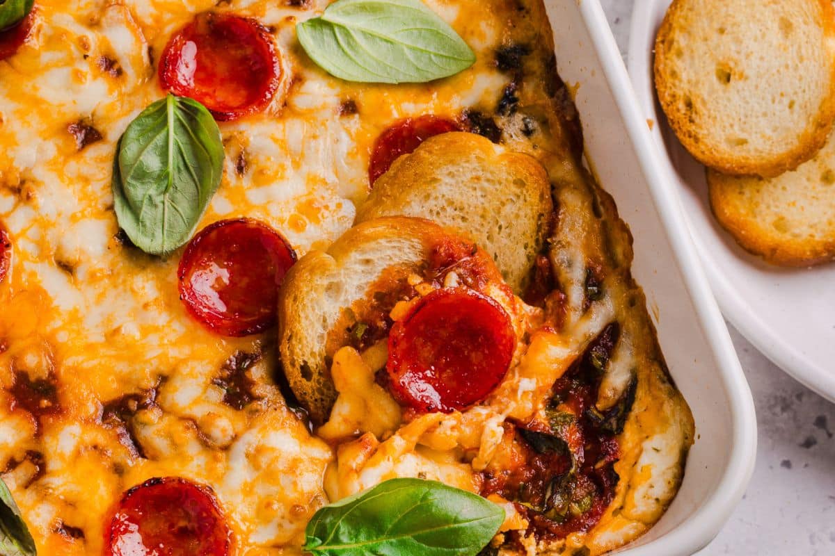 A square pan filled with pizza dip and two crostinis resting inside. 