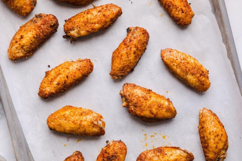 Baked honey garlic chicken wings on a parchment lined baking sheet before tossing with the sauce. 