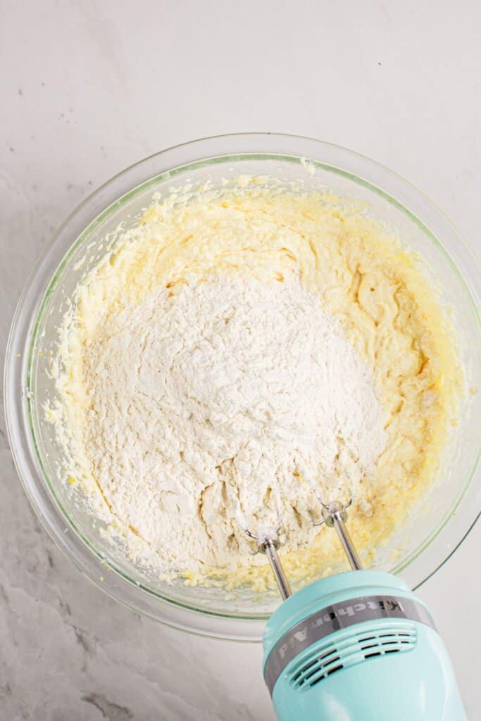 Flour being added to batter in a glass mixing bowl.