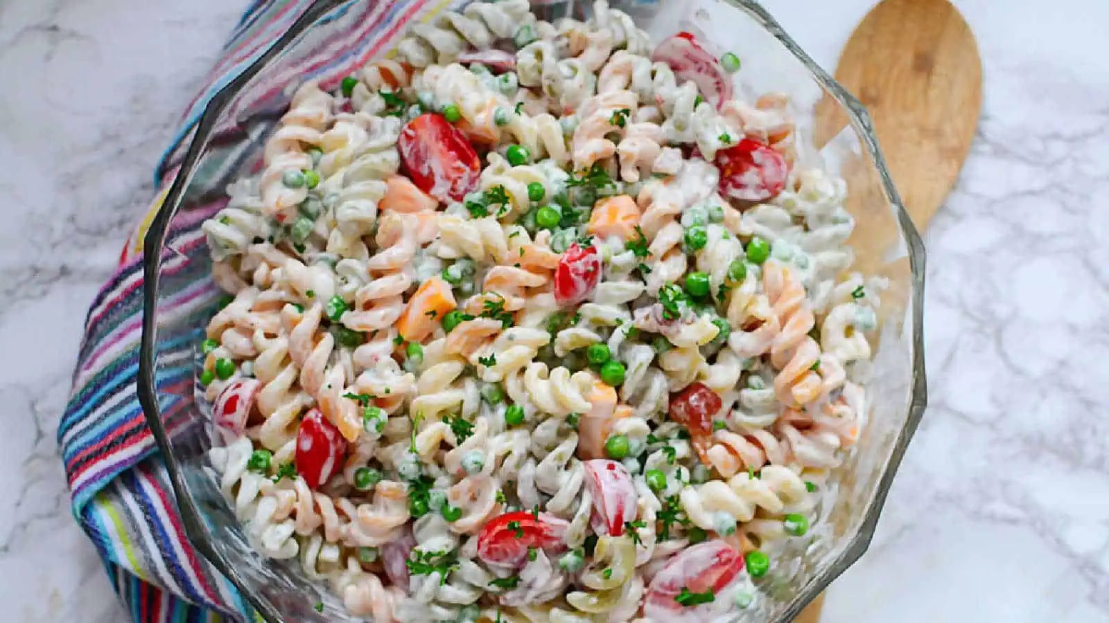 Pasta salad with peas and ham in a glass bowl.