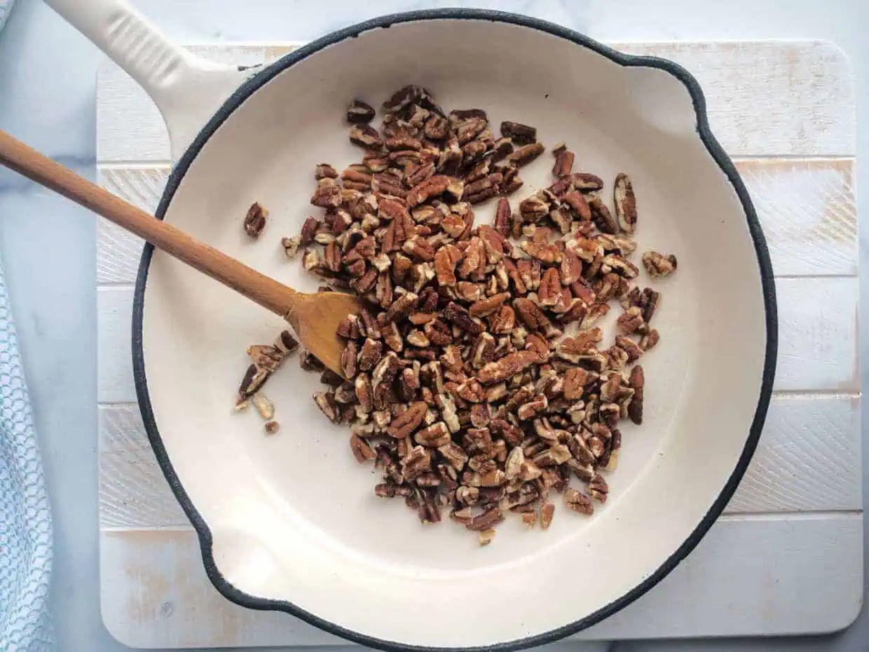 Pecans in a pan with a wooden spoon.