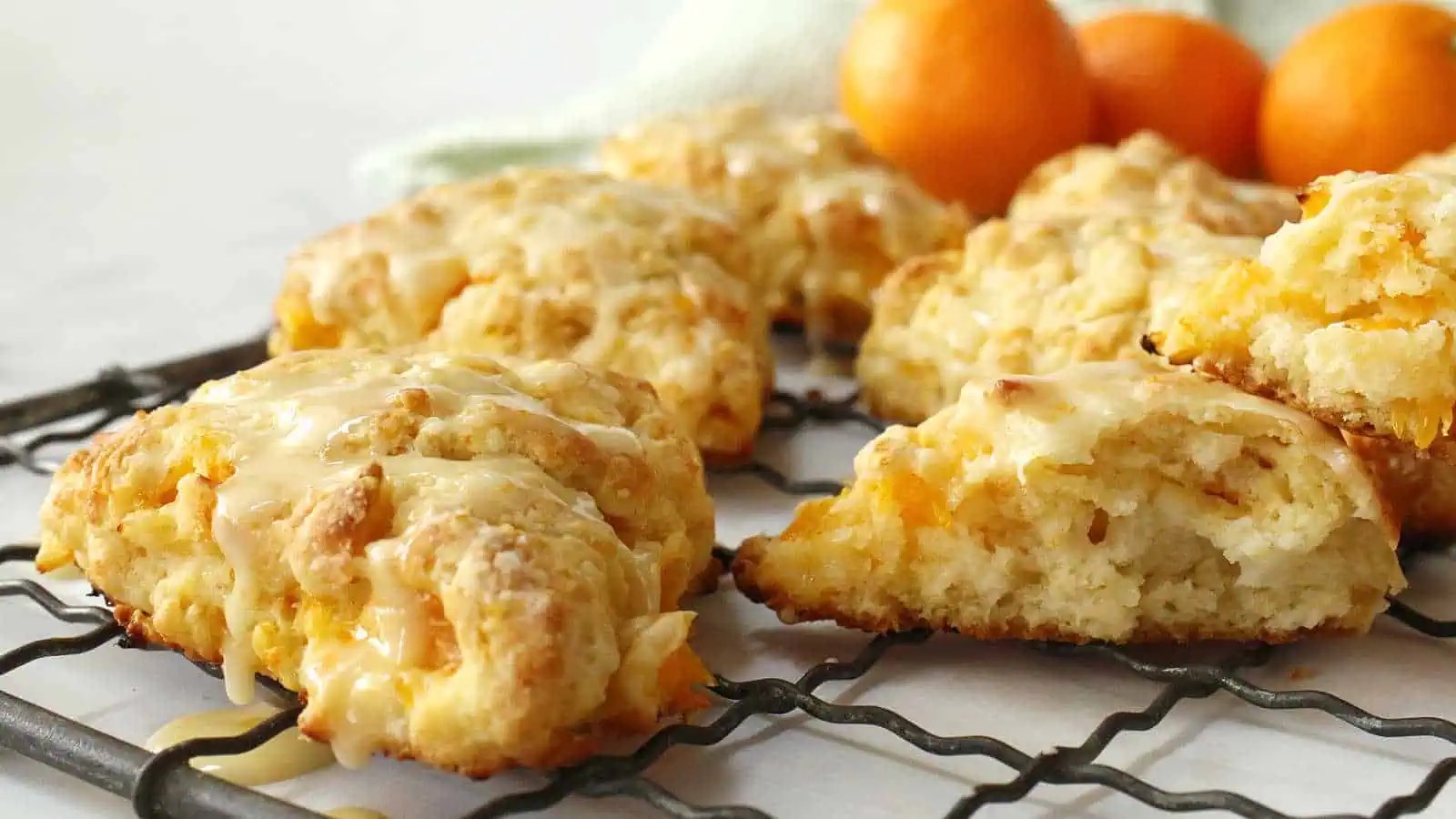 Orange scones on a cooling rack with oranges.