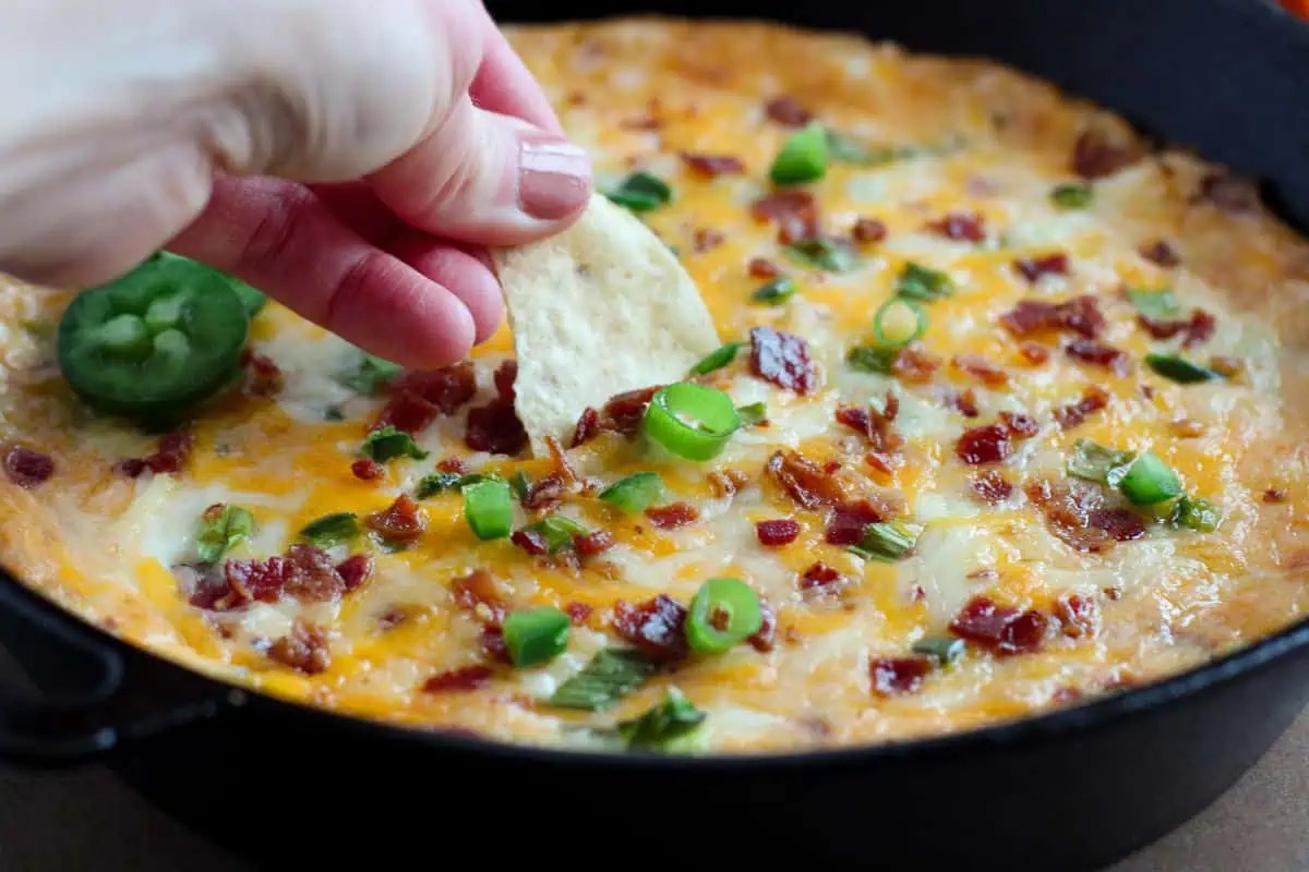A person dipping a chip into a skillet of dip.