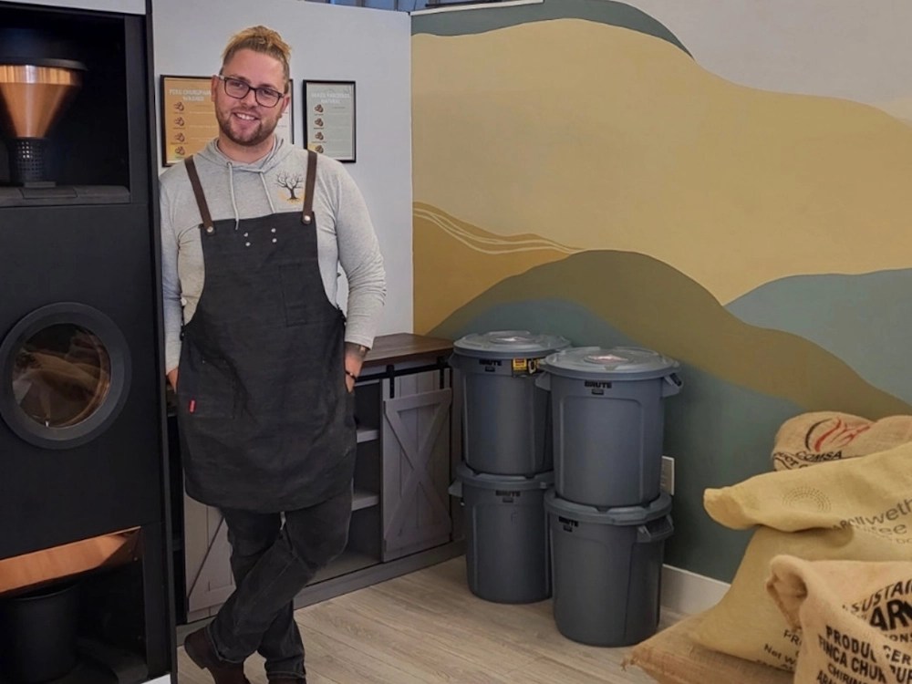 - Healthy Brew Hub Donovan Albert stands next to a Bellwether Shop Roaster at Anchor & Tree micro coffee roastery.