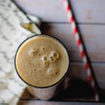 Date and Chikoo Smoothie served in a glass with a red and white straw on the side