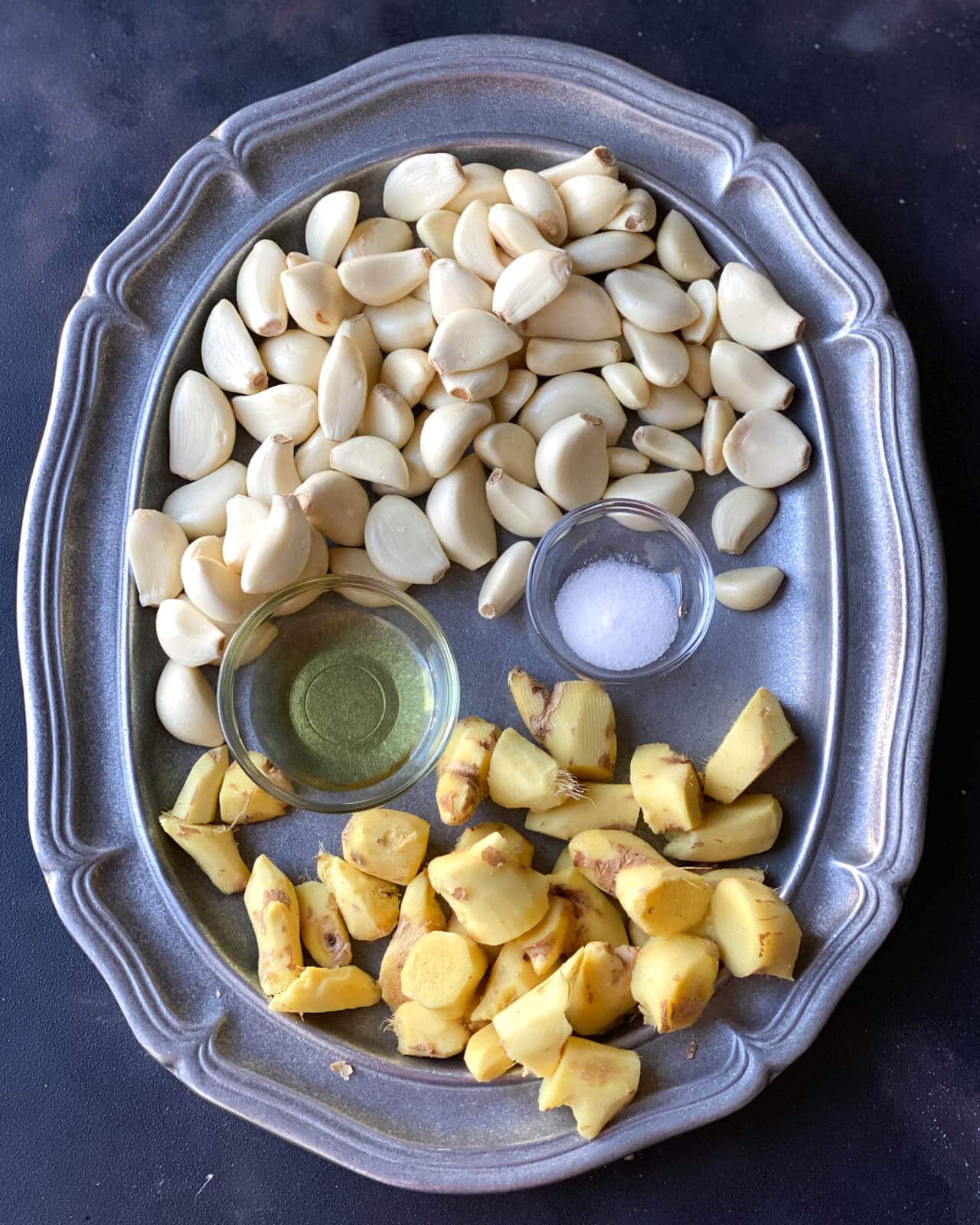 An overhead shot of garlic cloves, ginger, oil and salt