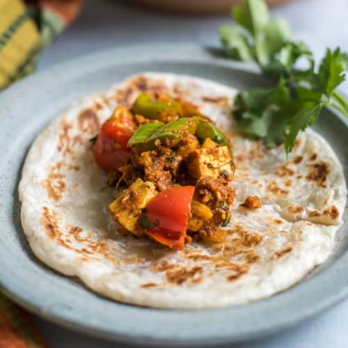 A blue plate with kadai paneer on a paratha with cilantro in the back.